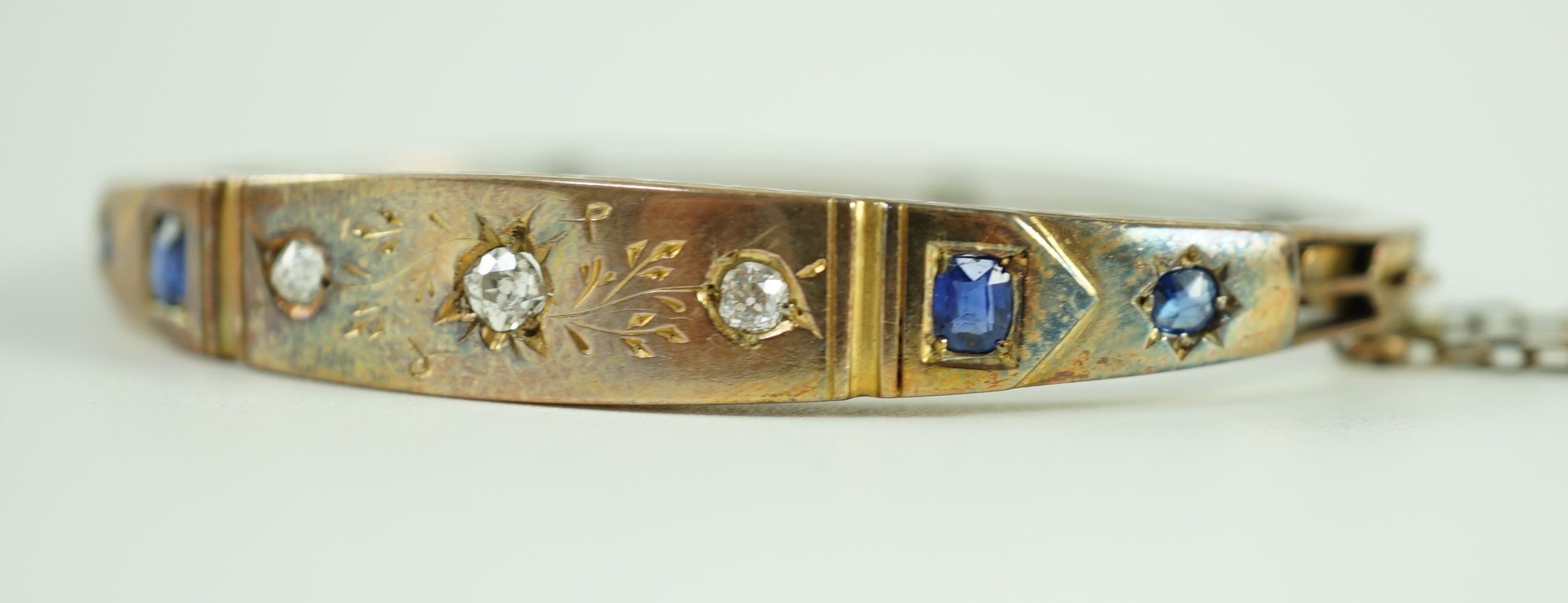 A late Victorian engraved gold, gypsy set three stone diamond and four stone sapphire set hinged bangle